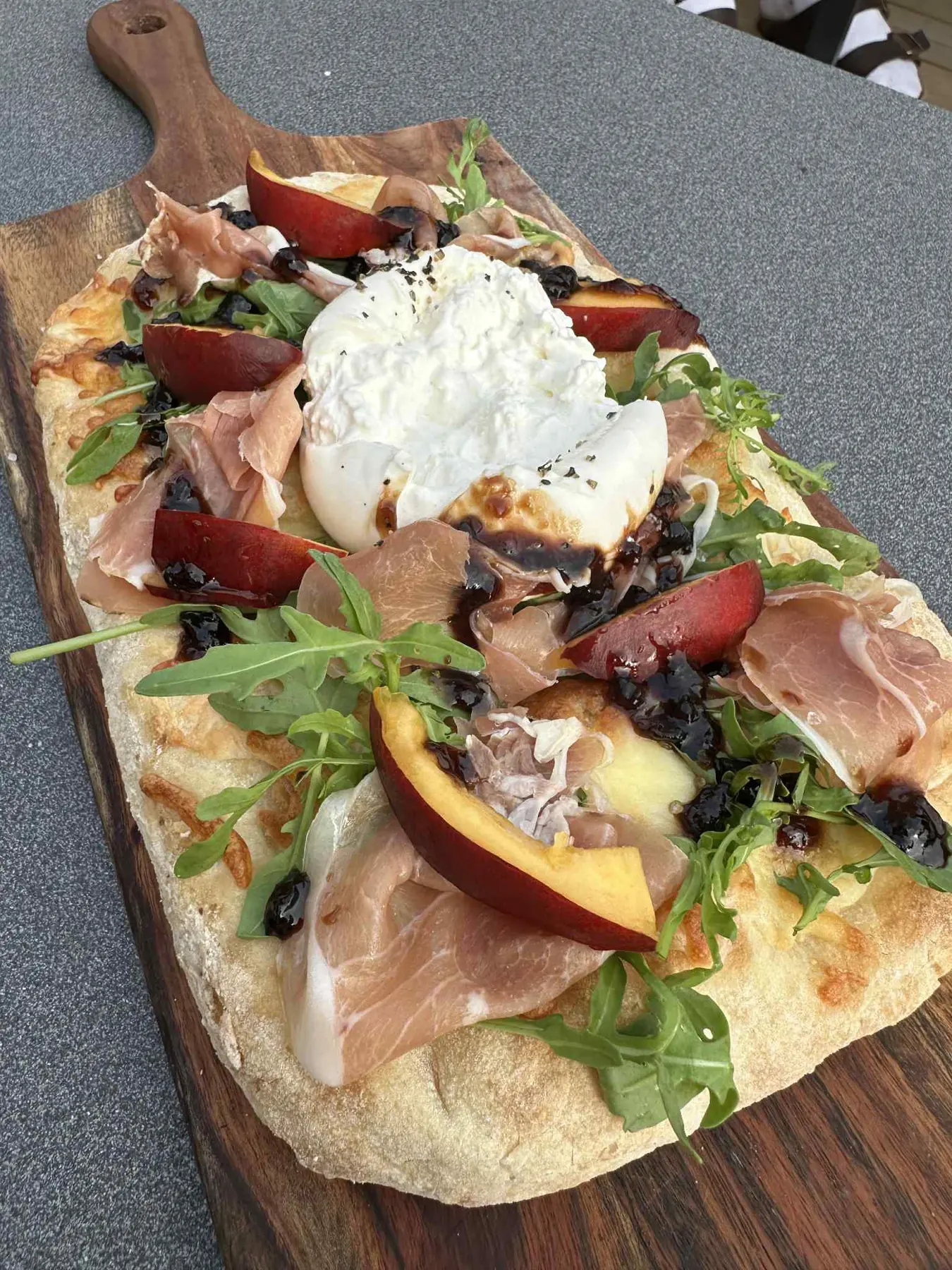 Surdejspizza med serrano, burrata og rucola på træbræt